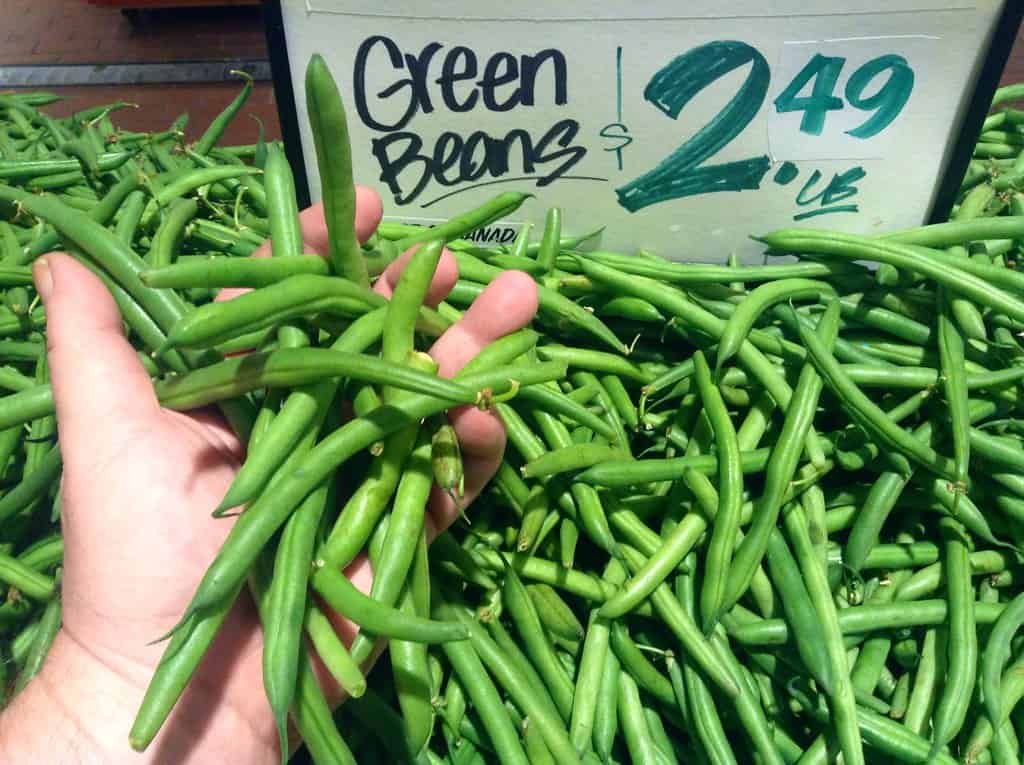A hand picking up fresh cut green beans in a farmers market, the perfect bean for Arkansas green beans
