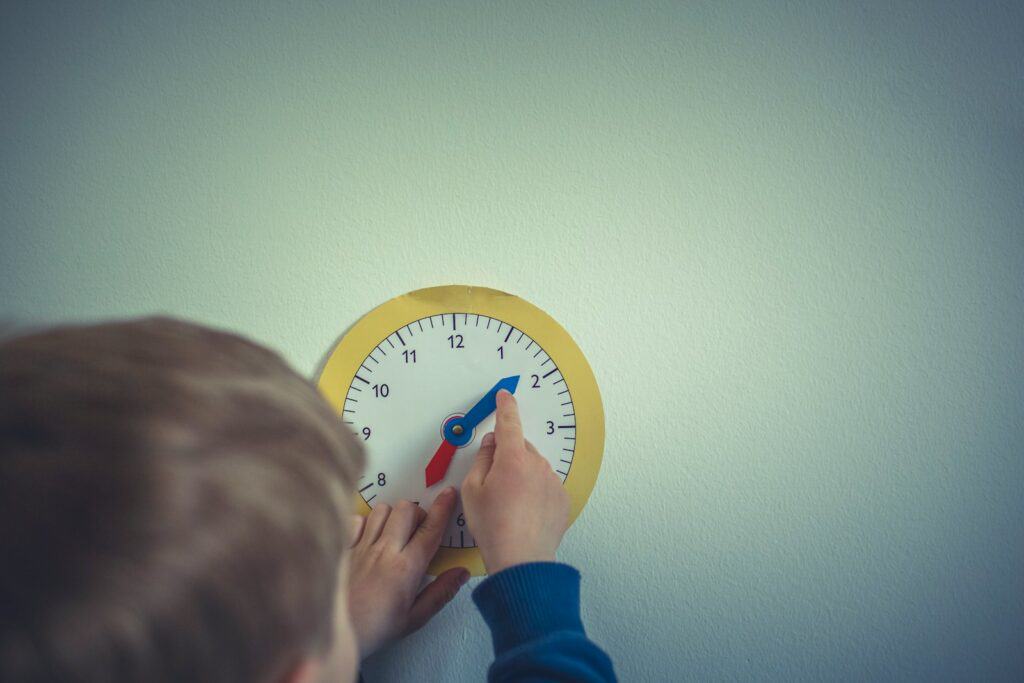 a child in blue long sleeves learning the basic life skill of using an analog clock