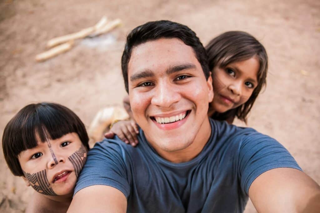 man in blue crew neck t-shirt smiling beside two children with face paint on a volunteer vacation