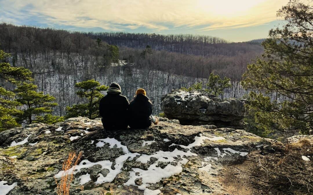 two people sitting on top of a rocky cliff during winter in Arkansas